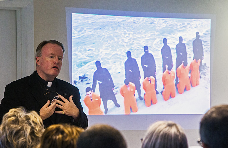 Father Benedict Kiely addresses the audience as a slide presentation displays Coptic Christians about to be martyred by beheading by Islamic terrorists in Lybia. The priest spoke Dec. 11, 2017 at St. Agnes Church, Key Biscayne, about the persecution of Christians in the Middle East.