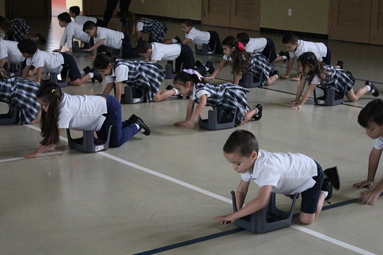 Los estudiantes de Kindergarten se estiran y dan golpecitos durante los ejercicios matutinos de NeuroNet Learning.