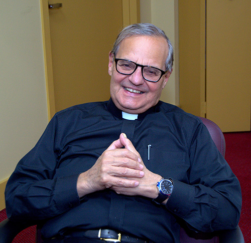 Mons. Franklyn M. Casale sentado en su oficina en la Universidad St. Thomas, Miami Gardens. Detrás está la entrada privada que nunca usa, ya que prefiere mantenerse abierto y visible a la comunidad universitaria. Planea retirarse esta primavera tras un cuarto de siglo como presidente de la universidad.