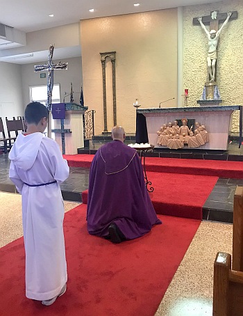 Seventh grader Vincent Alejo bears the processional cross as Father Luis Rivero kneels during a prayer service for victims of the shooting at Marjory Stoneman Douglas School.
