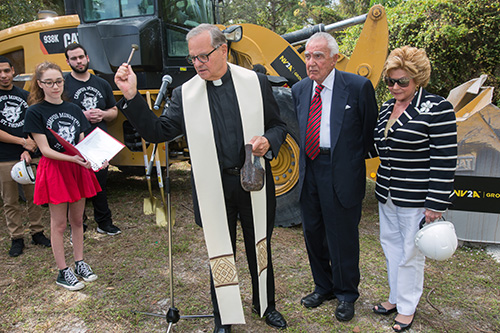 President Msgr. Franklyn Casale, St. Thomas University president, blesses the ground where new STU Business School complex will rise, as Gus and Lilliam Machado look on.