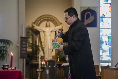 Father Thomas Liang, visiting priest from Shanxi Province in China, carries a fruit basket from the offering, at the conclusion of the Chinese New Year Mass and Ancestral Veneration at St. Jerome Church in Fort Lauderdale. At St right is Franciscus Chik, member of the Chinese Apostolate of the Archdiocese of Miami.