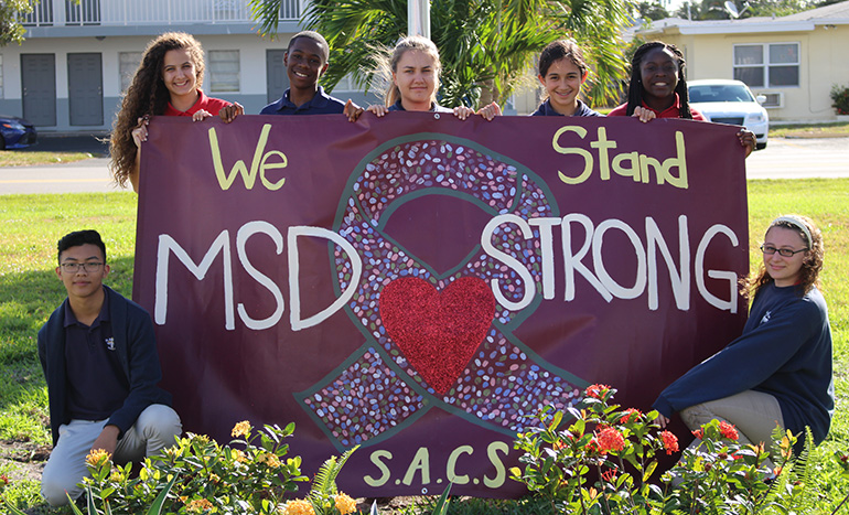 Students at St. Ambrose School in Deerfield Beach pose with the banner they created for students and staff at Marjory Stoneman Douglas High School in Parkland.