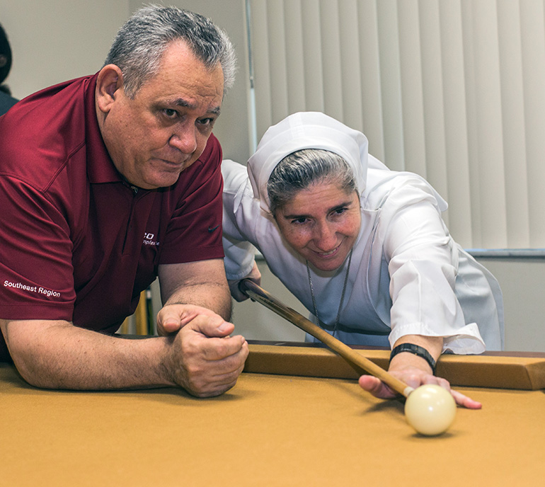 Professional billiard player John DiToro watches as Sister Filomena Mastrangelo, of the Sisters of St. Joseph Benedict Cottolengo, prepares to hit the ball with a cue.