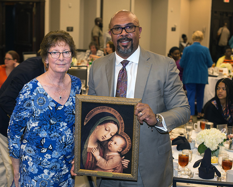 Mary Weber, chair of the MACCW Scholarship Committee, poses with Richard Jean, Archbishop Edward A. McCarthy High School principal, after presenting him him with an image of the Virgin Mary with Jesus.  Jean was this year's honoree as someone who has "made a difference" in Catholic education.