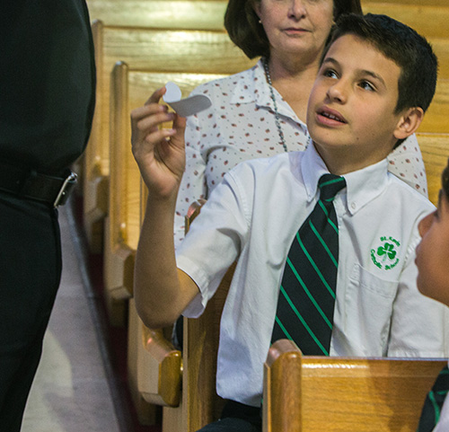 St. Kevin School sixth grader Tristan Trimino, 12, holds Father Luis Pavon's collar during the Focus 11 vocations rally March 1 at St. Agatha Church, Miami.