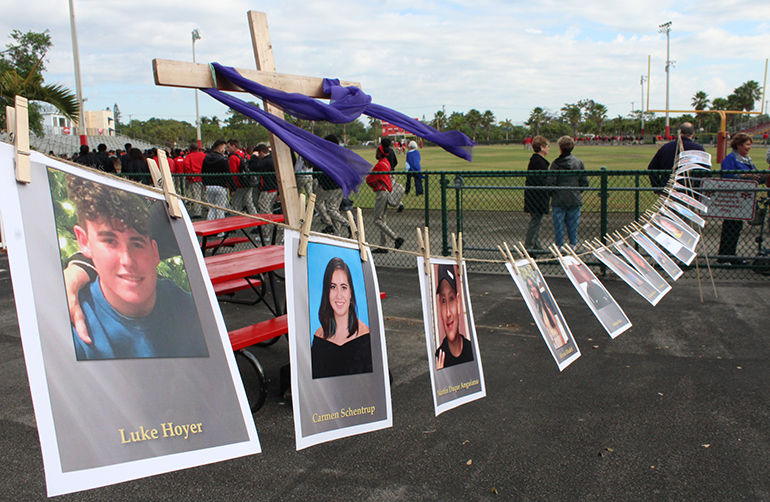 Pictures of the victims of the Marjory Stoneman Douglas High shooting hang on the entrance to the football stadium at Msgr. Edward Pace High. In the background stands a cross with the purple drapes of Lent.