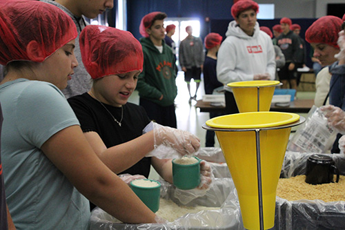 Fifth graders and cousins Sofia Lambert, a student at St. Patrick School, Miami Beach, and Kate Caballero, a student at Gulliver Prep, prepare their cups of rice for pouring into the meal bags.