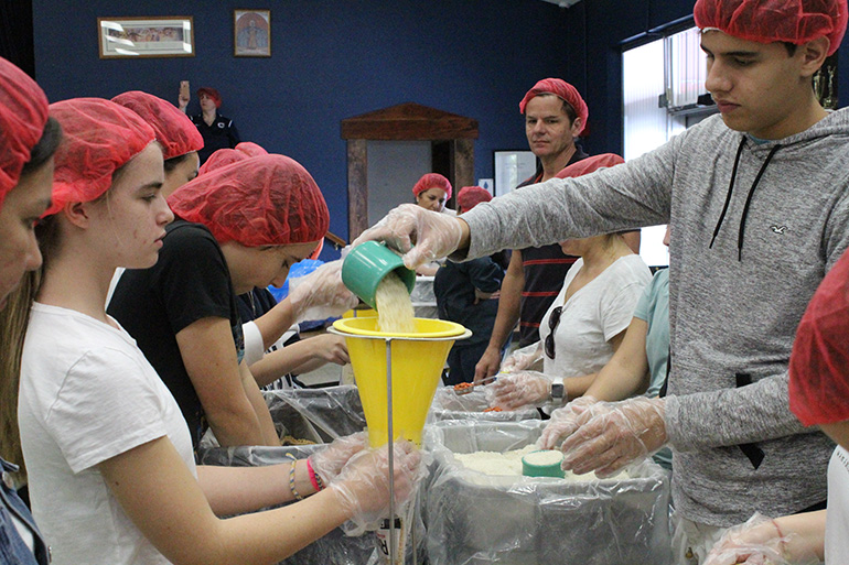 Students pour in rice, the final ingredient for a meal bag.