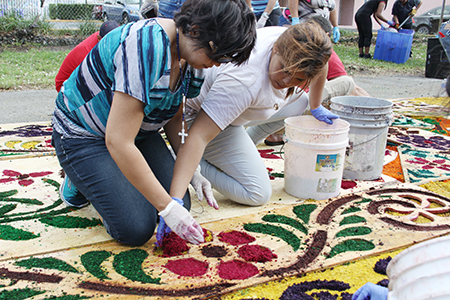 Dos voluntarias que ayudan a elaborar la alfombra para la procesión de Viernes Santo en la parroquia Corpus Christi rellenan con aserrín de colores las imágenes que fueron diseñas y cortadas en madera.