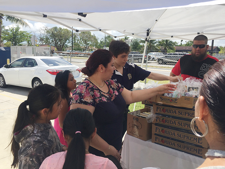 Mar&iacute;a Serrano, recepcionista de la Misi&oacute;n Santa Ana y coordinadora de la entrega de libros junto con Andr&eacute;s Alfonso, alumno del Colegio de Bel&eacute;n reparten los libros a los ni&ntilde;os que asistieron a la Misa el Domingo de Resurrecci&oacute;n. A la extrema derecha H&eacute;ctor Mart&iacute;nez, esposo de Serrano.