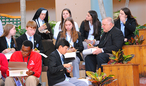 Archbishop Thomas Wenski joins Catholic high school students for a box lunch in the Pastoral Center atrium following the listening session. Here he sits with students from Archbishop Coleman Carroll High School in Miami.