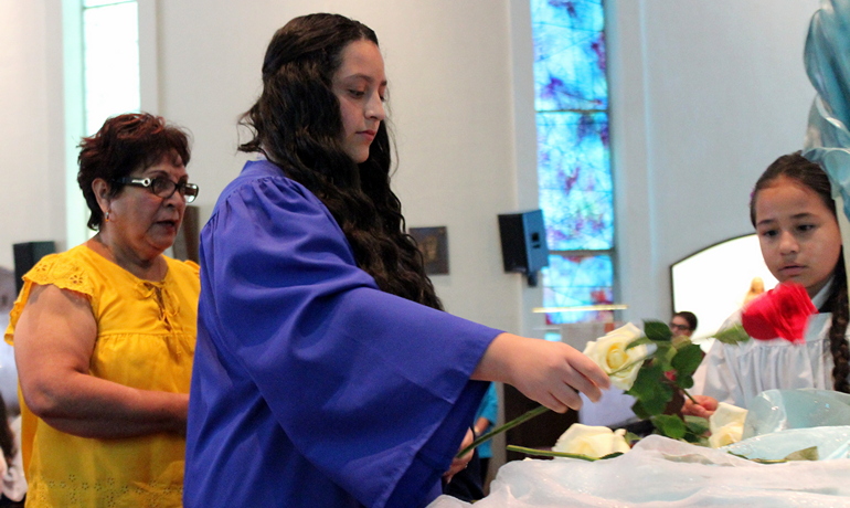 Hailey Sabillon lays a rose before an image of Mary during a Mother's Day Mass at St. Michael the Archangel. Taking part are altar server Ana Ghisays, right, and a grandmother from St. Michael's School. Both girls attend the school.