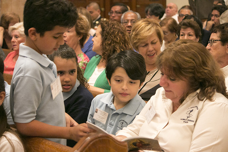 Rosie Di Lella, fifth grade religion teacher at St. Bonaventure School in Davie, sits with some of her students to await the ordination of the seminarian they "adopted," now Father Matthew Gomez. The trip to the ordination was completely voluntary and 18 of her 60 students attended. "They're leaning holy orders," Di Lella said, referring to the fifth grade curriculum which covers the sacraments. "So what better way than hands-on holy orders."