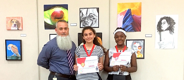 Two student artists show their awards during Pace High School's Gallery Night middle school competition. In the middle is Sarah Khoury of St. John the Apostle School, with Alexandra Creed of St. Bartholomew School on the right. At left is Marcel Navarro, lead instructor for Pace's Academy for Visual and Performing Arts.