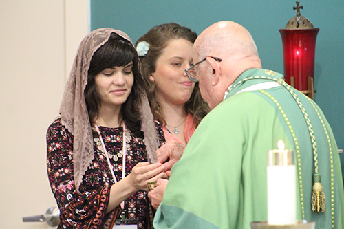 Elizabeth Rizzo, a consecrated virgin from New Orleans, receives Communion from Archbishop John Favalora. Next to her is Claire Halbur.