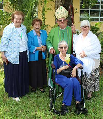 The consecrated virgins from the state of Florida pose with Archbishop Emeritus John Favalora; from left: Nancy Dvorak of the Diocese of St. Augustine, and Magalis Aguilera, Kathleen Danes (seated), and Maria de Los Angeles Exposito, all from the Archdiocese of Miami.