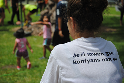 A volunteer watches activities on the the field. Her shirt reads in Haitian Creole, "Jesus I trust in you."