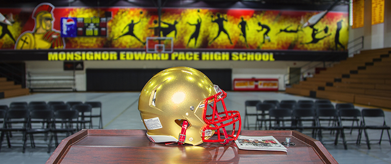A golden football helmet sits on a podium in the gym of Msgr. Edward Pace High School.
