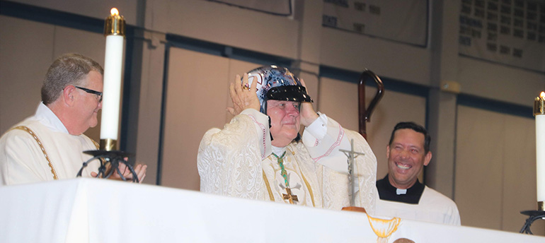 Archbishop Thomas Wenski tries on his new "Adelante"-branded motorcycle helmet after celebrating an all-school Mass Aug. 30 to mark the start of the 60th school year at the Marist Brothers' Christopher Columbus High School in Miami. Looking on, from left: Deacon James Dugard, Columbus theology teacher, and Father Richard Vigoa, the archbishop's master of ceremonies.