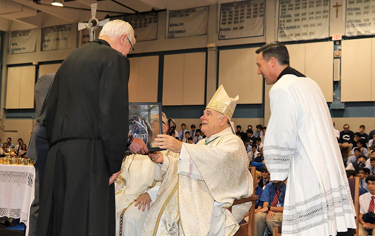 Marist Brother Kevin Handibode, president of Christopher Columbus High School, presents Archbishop Thomas Wenski with an "Adelante"-branded motorcycle helmet after the all-school Mass Aug. 30 to mark the start of the 60th school year at the Miami school. Looking on, right, is Father Richard Vigoa, the archbishop's master of ceremonies.