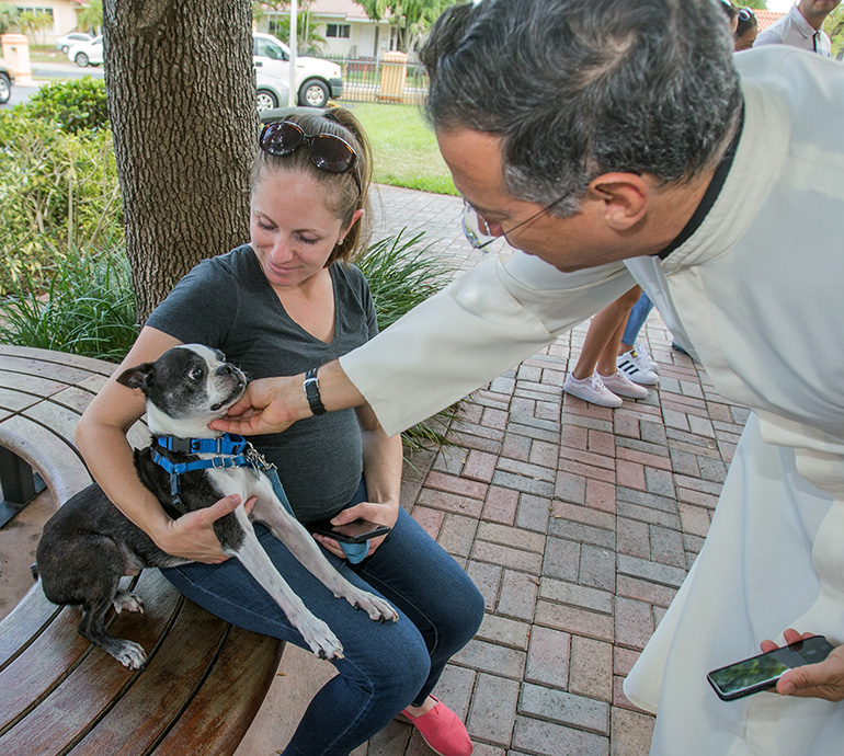 Father Manuel Puga, parochial vicar at St. Rose of Lima, pets "Rodney," a Boston terrier, as his owner, Erin Halloran, looks on.