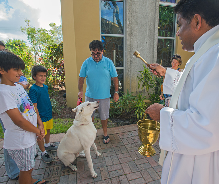 Father George Packuvettithara, St. Rose of Lima pastor,  blesses "Lupo," a white German Shepherd, as Salvador Barreiros and his family look on.