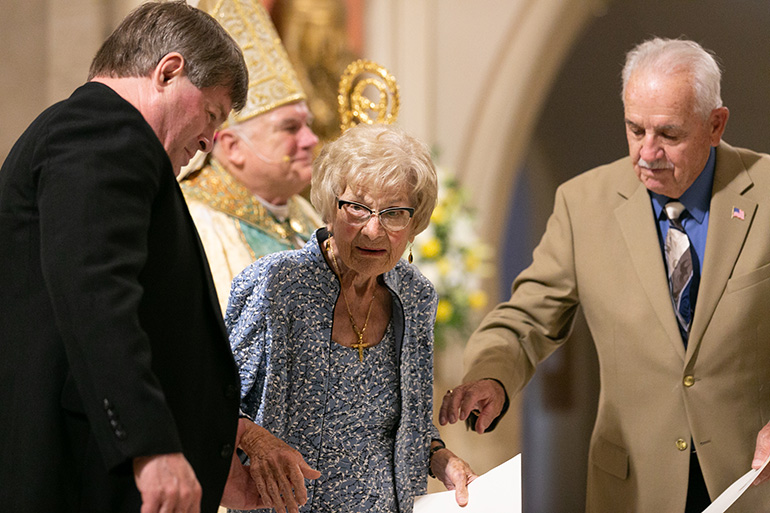 Rose Preseau, de 101 años, regresa del altar después de haber sido recibida por el Arzobispo Thomas Wenski. La acompañan el también homenajeado Jubilaeum, John Frink y su párroco, el P. Steve O’Hala.