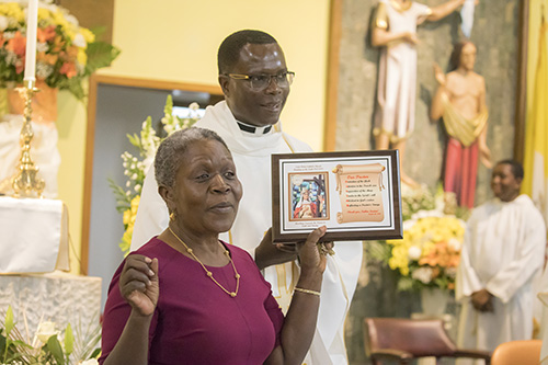Marcelle Chery, parish manager at St. Helen, gives Father Lucien Pierre, the parish's administrator, a plaque commemorating the church's golden jubilee and his contributions as pastor.