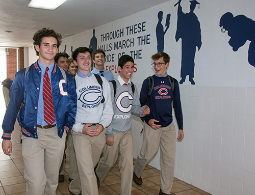 Un grupo de estudiantes de Christopher Columbus circula por un pasillo del colegio, pasando frente a un mural donde se lee, "Por estos pasillos circula el orgullo de los Exploradores".