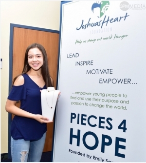 Emily Sanudo poses by a poster for Pieces 4 Hope, the jewelry company she founded to benefit a local charity.