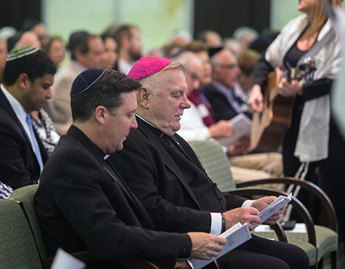 Archbishop Thomas Wenski and his priest-secretary, Father Richard Vigoa, listen to cantorial soloist Jodi Rozental play the guitar and sing during the Shabbat service at Temple Judea.