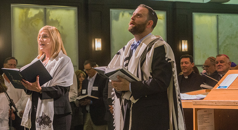 Cantorial soloist Jodi Rozental and Rabbi Jonathan Fisch, holding prayer books, lead the congregation in prayer as Father Richard Vigoa, archbishop's priest secretary, and Archbishop Thomas Wenski look on in the background.