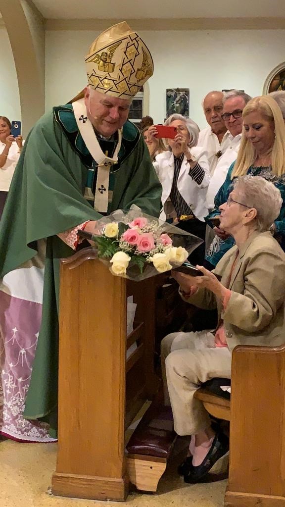 Archbishop Thomas Wenski presents a bouquet of flowers to Myrna Gallagher, who together with Father David Russell, then pastor of St. Louis in Pinecrest, started the Emmaus retreats in the archdiocese in 1978. The movement marked its 40th anniversary with a Mass Nov. 3 at St. Mary Cathedral.