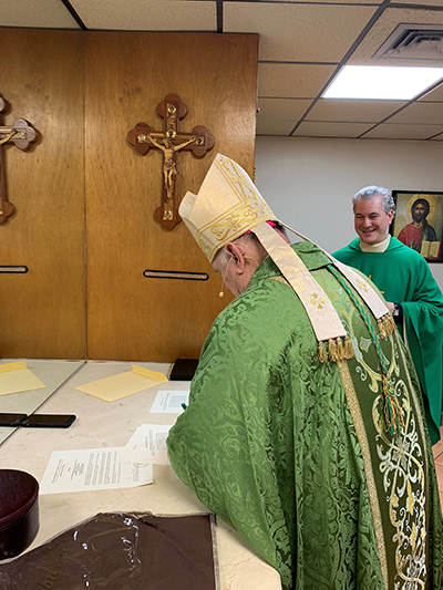 El Arzobispo Thomas Wenski firma los papeles que hacen oficial el nombramiento  del P. Lazarus Govin, a la derecha, como párroco de la iglesia St. Martha en Miami Shores.