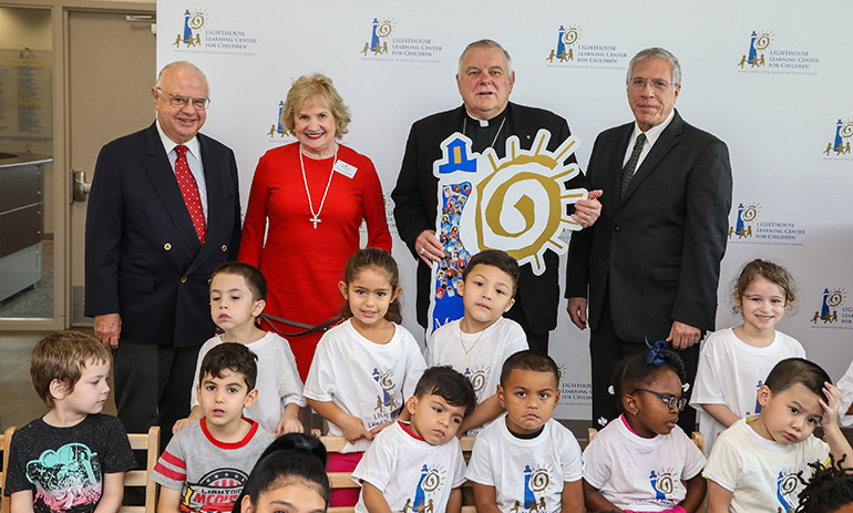 Archbishop Thomas Wenski poses with Miami Lighthouse for the Blind president and CEO Virginia Jacko, board members John Harriman, far left, and Ray Casas, far right, and pre-kindergarten children who presented him with their Lighthouse tribute gift during his visit, Nov. 8, 2018.