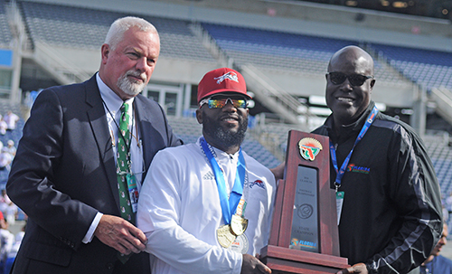 Chaminade-Madonna coach Dameon Jones, center, accepts the state-championship trophy from FHSAA Executive Director George Tomyn, left, and FHSAA board member Herschel Lyons.