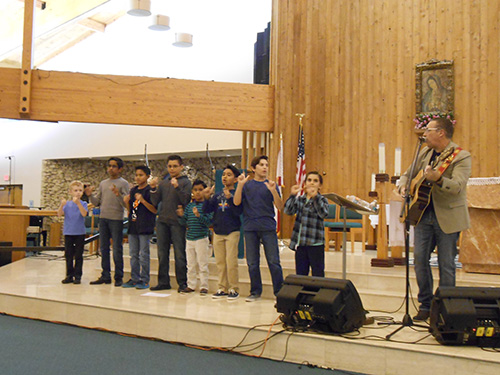 Steve Angrisano invites young people to join him in leading attendees with hand movements to the song, "Trading my Sorrows," during his concert Nov. 16 at St. Andrew Church in Coral Springs.