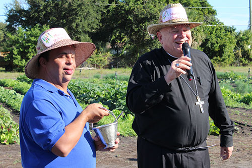 El Arzobispo Thomas Wensk dice unas palabras después de bendecir el campo y la granja orgánica urbana en el Marian Center. Lo asiste el integrante del programa de Capacitación Diurna del Centro Mariano, Christopher Abreu.