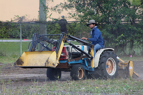 El alegre granjero Moses Kashem ara la tierra del Marian Center con un tractor para producir más productos en la granja urbana.