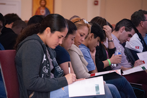 Members of St. John XXIII's youth and young adult groups, armed with pens and a program booklet, take notes during Christopher West's talk.