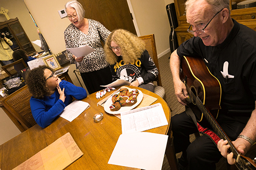 Father Liam Quinn, new pastor of St. Gabriel Parish in Pompano Beach, sings Christmas carols after decorating a holiday gingerbread man Dec. 22. Behind him are Tiffany and Ashley Hayes and their grandmother, Debbie McEachern.