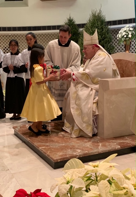 Archbishop Thomas Wenski receives offertory gifts from a young member of Miami's Filipino community during the final Simbang Gabi Mass of 2018, celebrated Dec. 23 at St. Rose of Lima, Miami Shores.