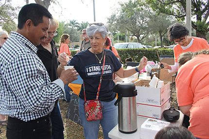 Un inmigrante hondureño, que llegó recientemente de su país, toma café mientras espera su hora de entrada a su cita de inmigración. A la derecha, Silvia Muñoz del Instituto Pedro Arrupe de Miami.