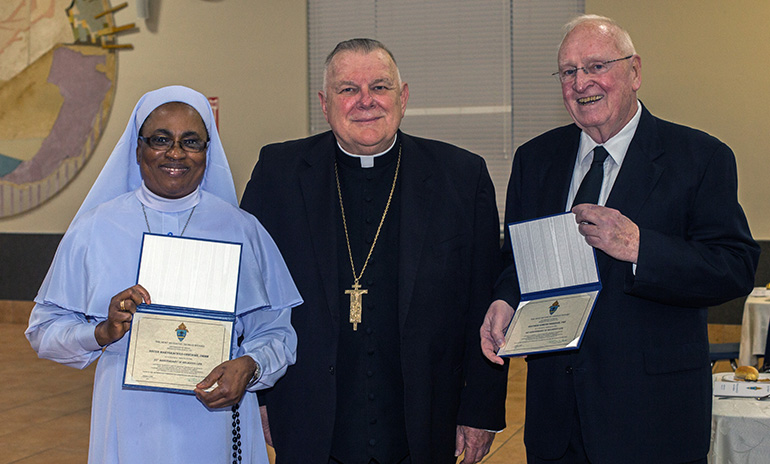 La Hna. Marygracious Onwukwe, de las Hijas de María, Madre de la Misericordia, y el Hno. Marista Edmund Sheehan, posan con el Arzobispo Thomas Wenski y los certificados que recibieron para conmemorar sus jubileos número 25 y 60, respectivamente.