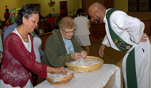 “Take as many as you want,” Father Roy Lee says to those who line up for small stones and sets of wings during a revival at St. Bernard Church presented by the archdiocesan Office of Black Catholics.