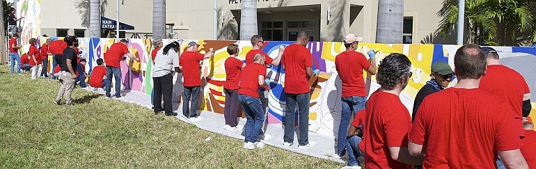 Workers paint a 100-foot mural at Camillus House in Miami. Wearing red shirts are workers from the Dow Chemical Company, with black shirts on Camillus House staffers.