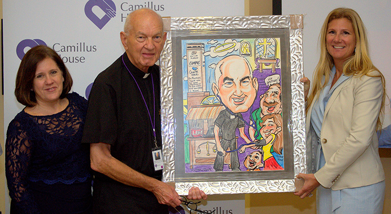 Officers of Camillus House present Hospitaller Brother Raphael Mieszala with an affectionate caricature after his farewell Mass at the shelter for the homeless. With him are CEO Hilda Fernandez, left, and Andria Hanley, vice president of development.