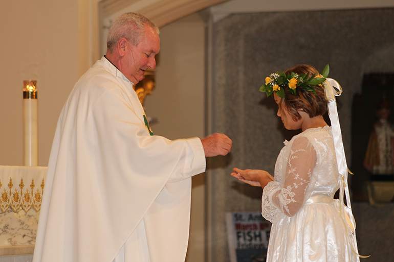 Father Michel Grady, pastor of St. Anthony Parish in Fort Lauderdale, distributes the Eucharist to Sophia Oberhelman, 10.