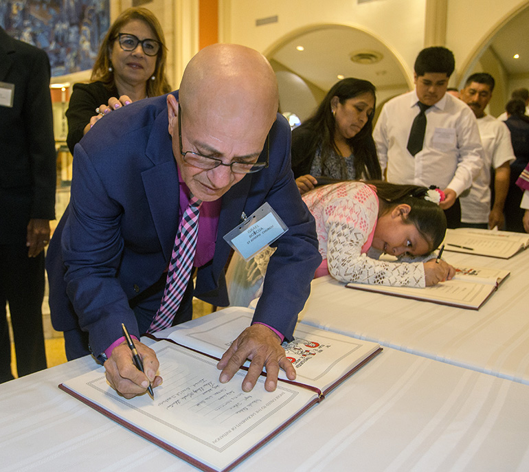 Israel Boicija, from St. Joseph Church, Miami Beach, signs the Book of the Elect as his sponsor, Carrie Parrilla, stands behind him.